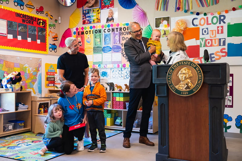 Man holding baby behind podium with people surrounding him