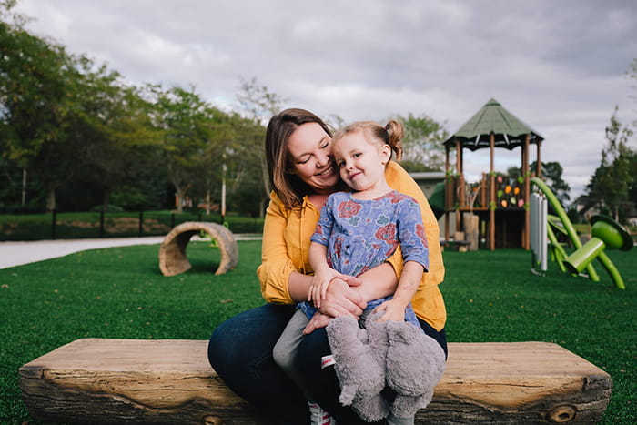 A Mother and young daughter sit together on an outdoor playground 