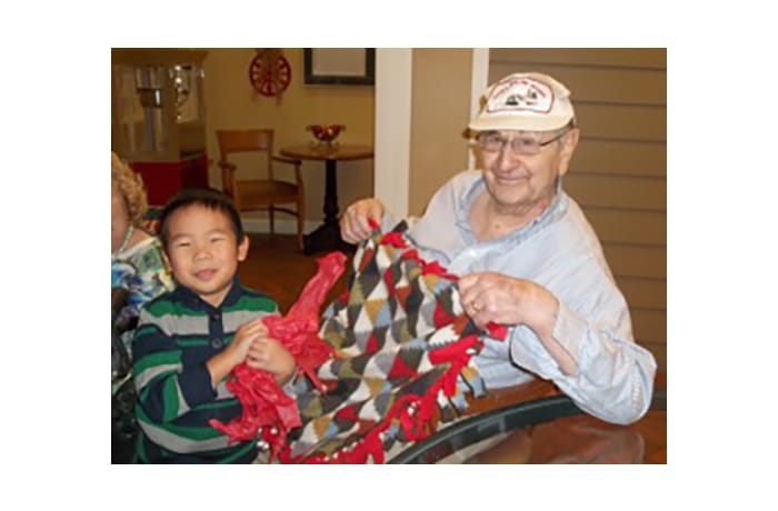 Child and elderly man displaying handmade blanket