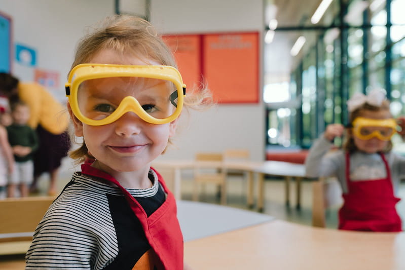 Child wearing apron and goggles while sitting at table